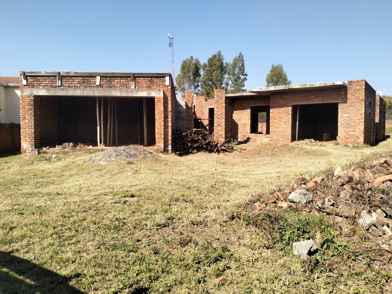 Rear view of a property currently under construction, featuring exposed brickwork and concrete structural elements on a large plot.