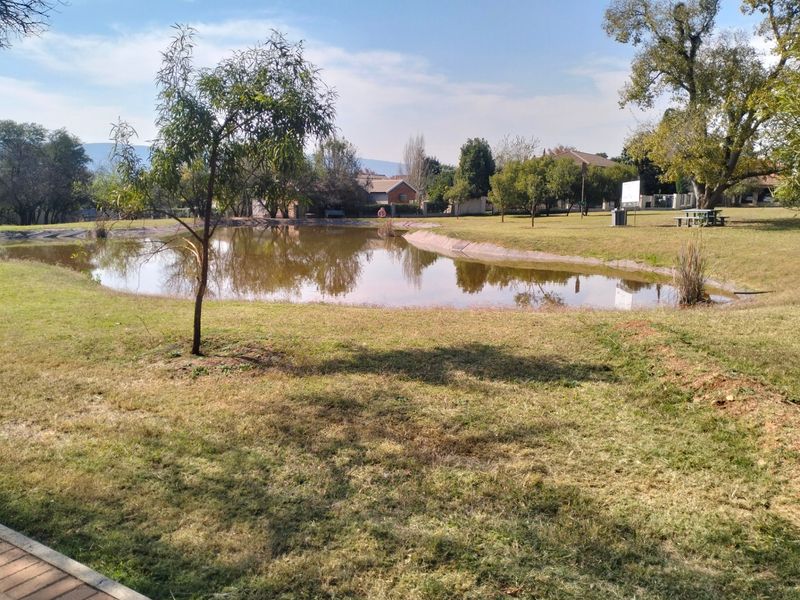 A peaceful garden area featuring a large man-made pond surrounded by landscaped lawns and mature trees, providing a scenic outdoor space.