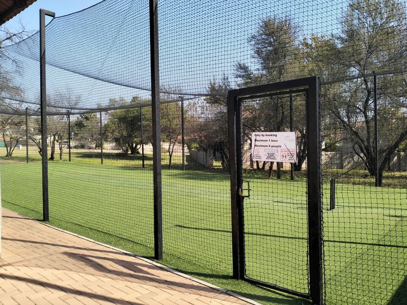 A fenced outdoor sports facility featuring artificial turf and perimeter netting, suitable for cricket practice.