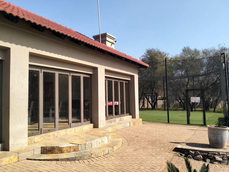 Rear exterior view featuring a paved patio, stone-clad steps, and large stacking glass doors leading into the home, adjacent to a netted sports area.