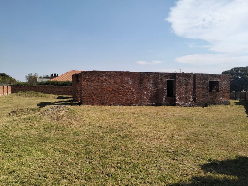 A view of an unfinished brick structure situated on a large plot of land, showing the building shell and surrounding yard.