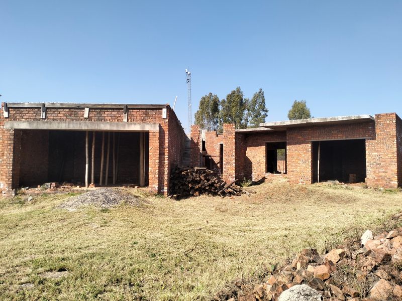 A rear view of a residential property currently under construction, featuring exposed brickwork and concrete structural elements in an unfinished state.