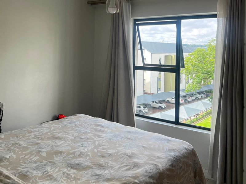 A bedroom featuring tiled flooring, a large aluminium-framed window with curtains, and a central pendant light fixture.