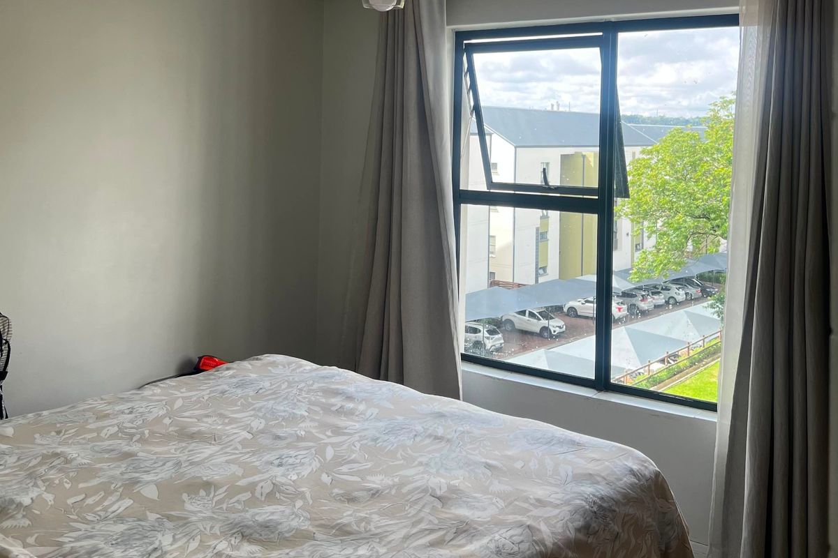 A bedroom featuring tiled flooring, a large aluminium-framed window with curtains, and a central pendant light fixture.