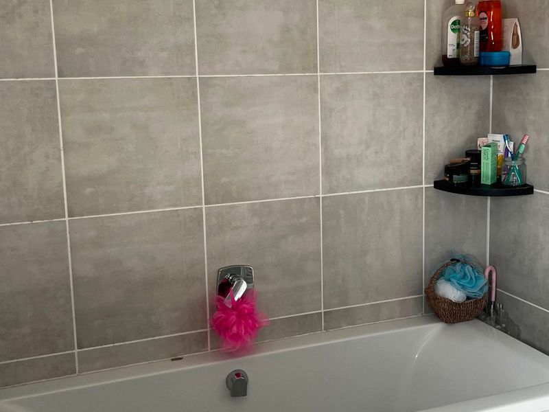 A clean bathroom featuring a white bathtub with wall-mounted mixer tap and neutral grey ceramic wall tiling.