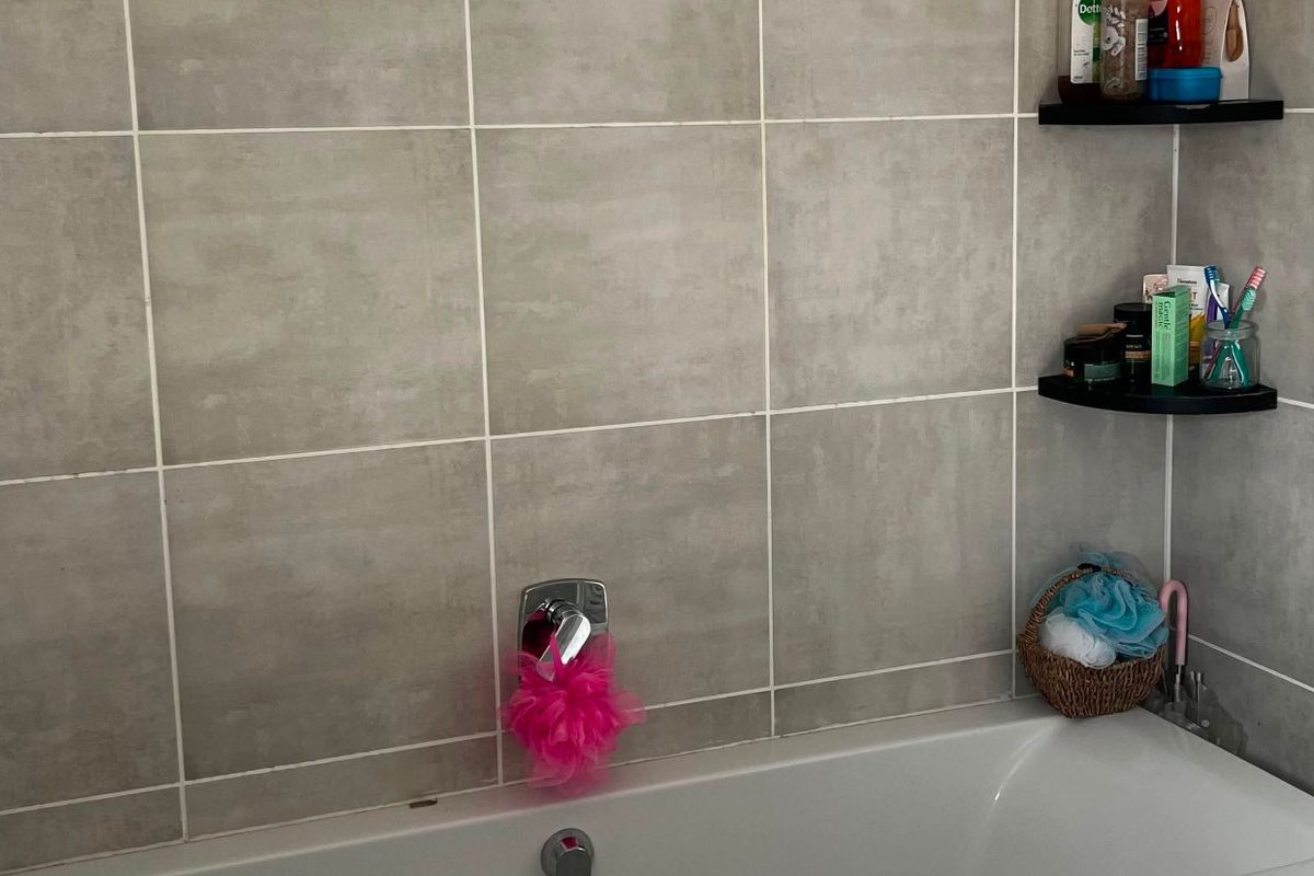 A clean bathroom featuring a white bathtub with wall-mounted mixer tap and neutral grey ceramic wall tiling.