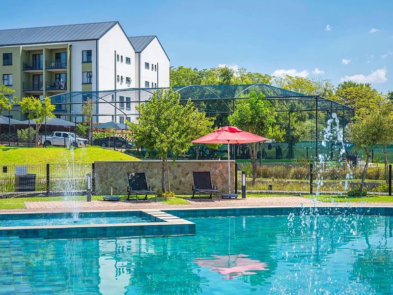 A well-maintained communal swimming pool area featuring a water fountain, stone retaining wall, and paved deck, set within a landscaped residential estate.