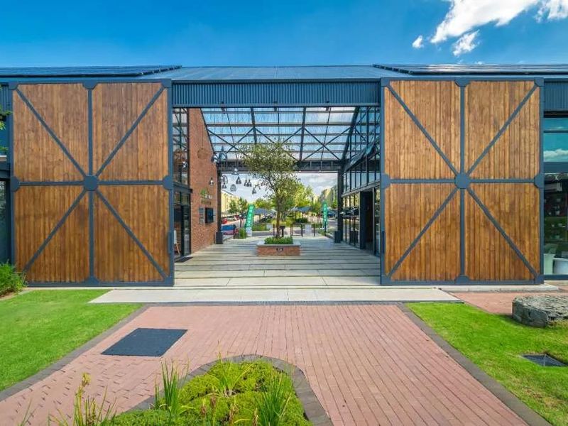 Modern apartment complex entrance featuring large timber barn-style doors, a covered walkway, and well-maintained landscaped grounds.