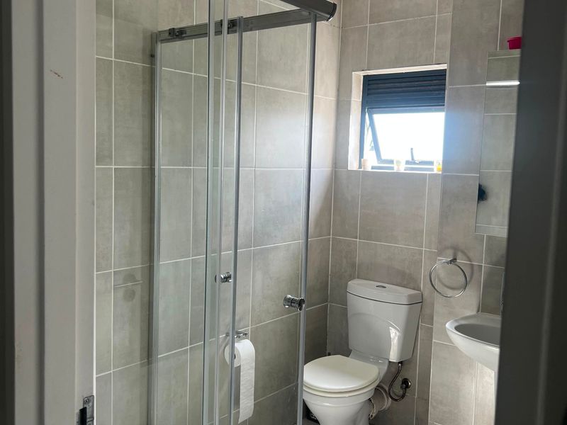 A functional bathroom featuring a glass shower enclosure, pedestal sink, toilet, and neutral grey ceramic tiling throughout.