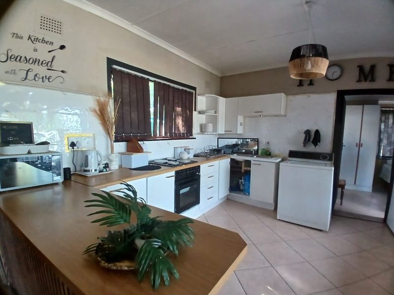 A functional kitchen featuring white cabinetry, an electric oven and hob, tiled flooring, and a breakfast bar, with some minor maintenance required.