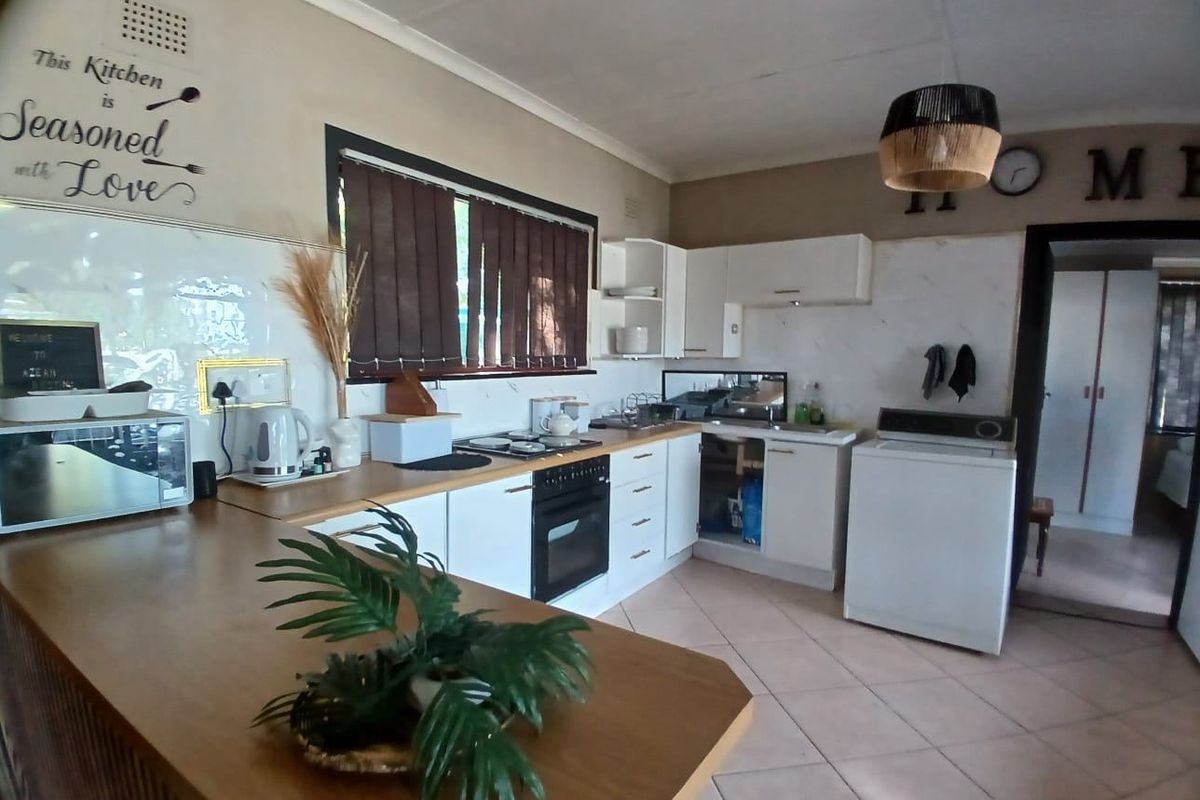 A functional kitchen featuring white cabinetry, an electric oven and hob, tiled flooring, and a breakfast bar, with some minor maintenance required.