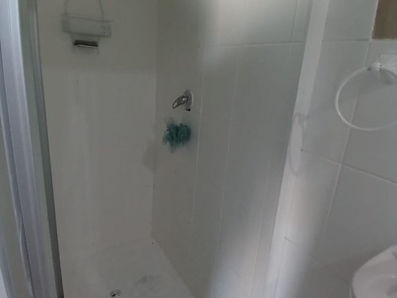 A compact shower enclosure featuring white wall tiles, a modern square shower head, and a standard shower tray.