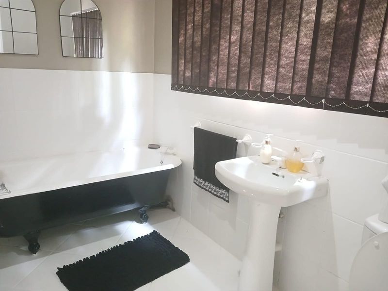 A functional bathroom featuring a classic clawfoot bathtub, pedestal basin, and neutral wall tiling with vertical window blinds.