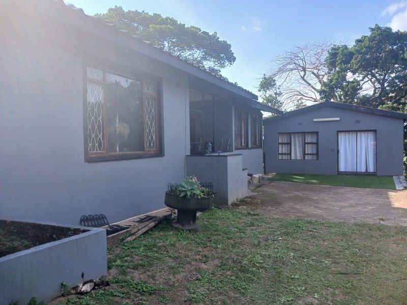 Rear view of the property showing a main house structure with security bars, a paved patio area, and a separate outbuilding with a tiled roof.