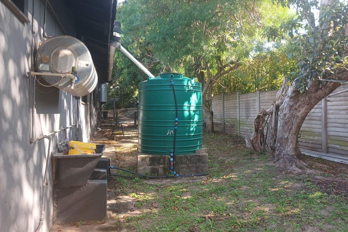 Rear exterior area featuring a large water storage tank on a concrete plinth, external geyser, and a concrete wash trough against the house wall.