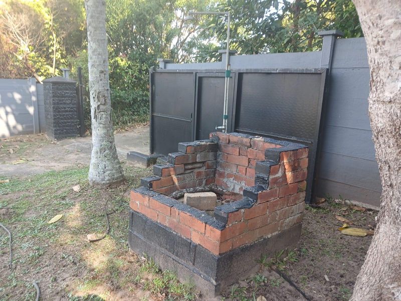 Outdoor garden area featuring a brick braai structure and an external shower fixture set against a boundary wall.