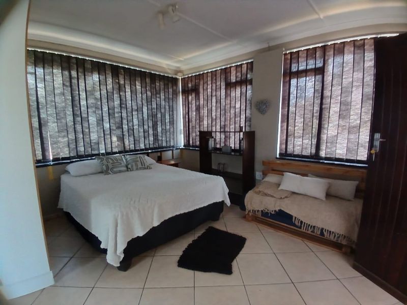 A spacious bedroom featuring tiled flooring and extensive window coverage with vertical blinds, offering a functional layout.