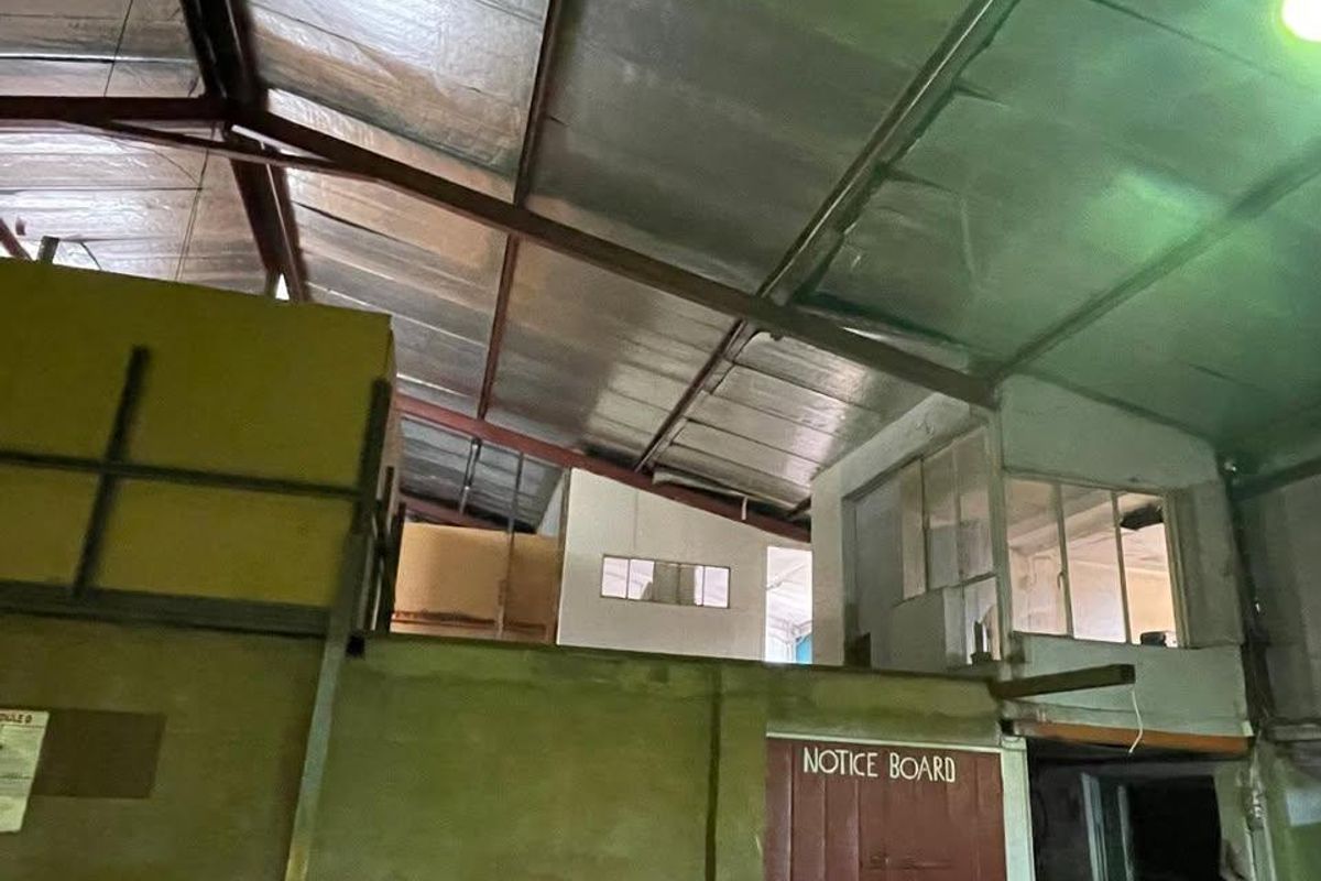 Industrial warehouse space featuring high ceilings with exposed steel trusses, foil insulation, and an integrated mezzanine office area.