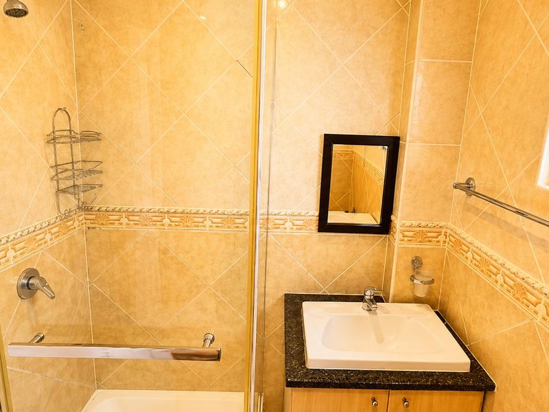 A functional bathroom featuring a shower enclosure, vanity cabinet with granite countertop, and decorative ceramic wall tiling with a window security gate.