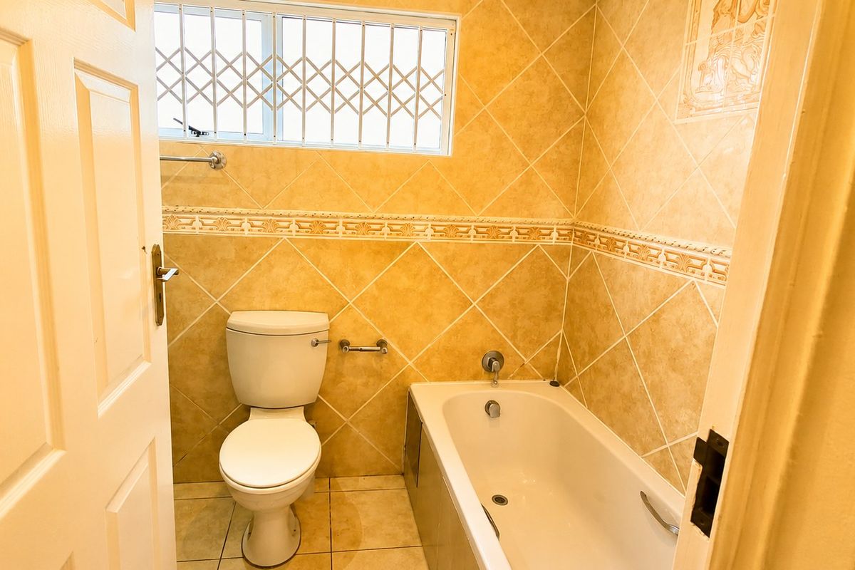 A functional bathroom featuring a bathtub, toilet, and tiled wall finishes with a security gate on the window.