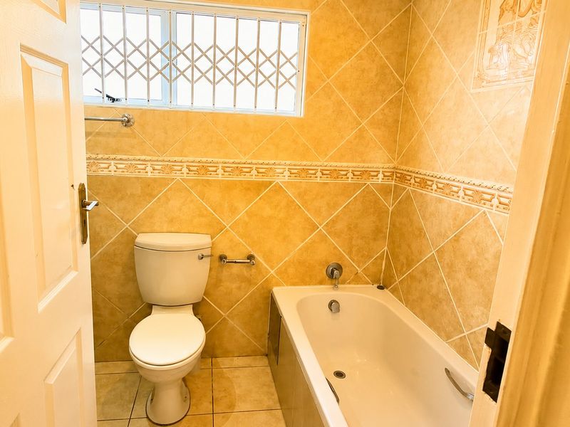 A functional bathroom featuring a bathtub, toilet, and tiled wall finishes with a security gate on the window.