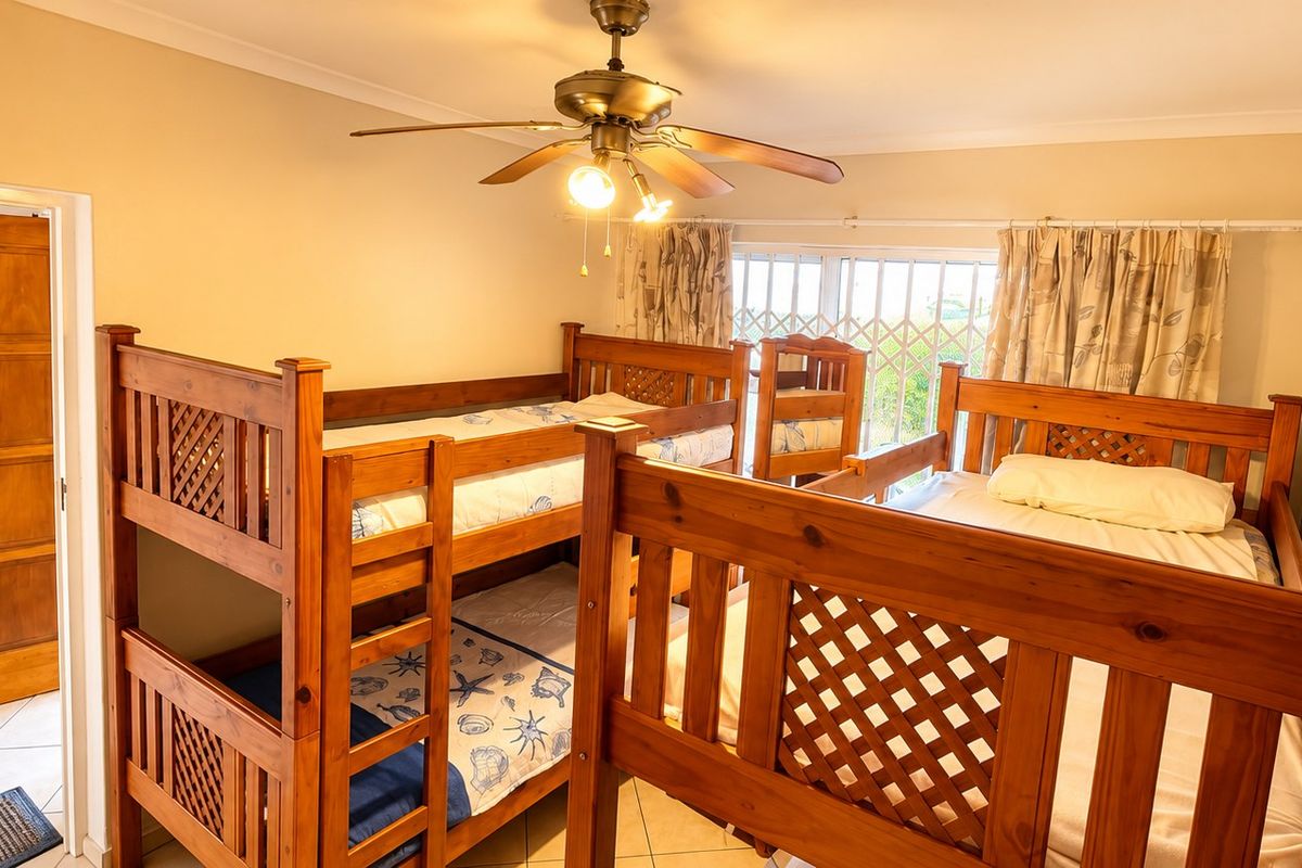 A bedroom featuring tiled flooring, a ceiling fan, and a security gate over the window, currently configured with multiple wooden bunk beds.