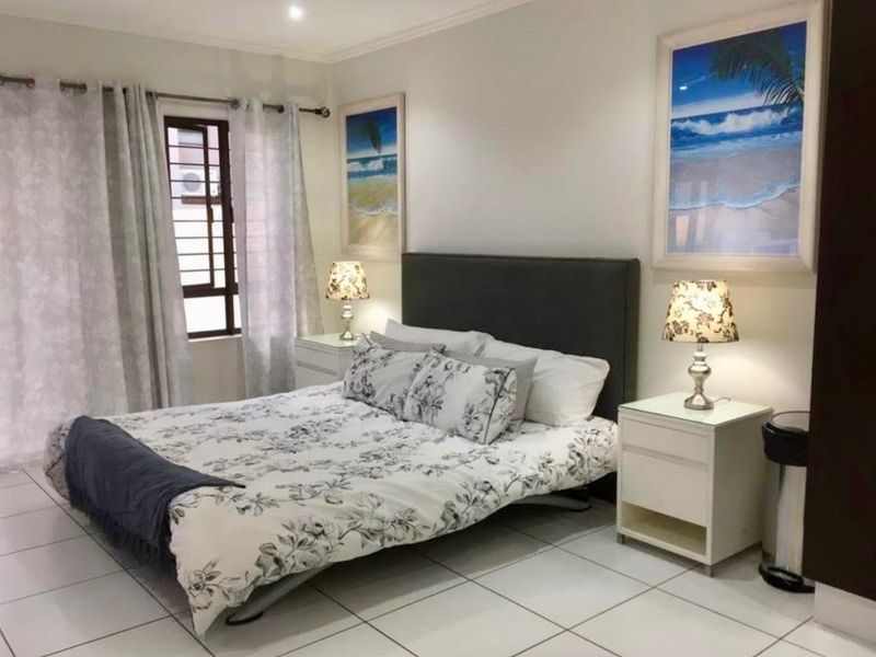 A well-maintained bedroom featuring neutral tiled flooring, recessed ceiling lighting, and a window fitted with security bars for added peace of mind.