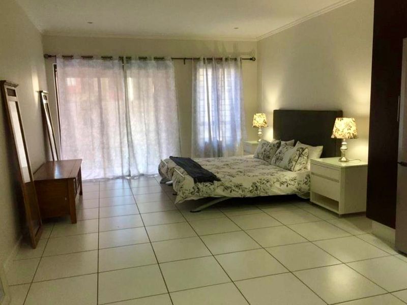 Spacious bedroom featuring neutral tiled flooring, recessed lighting, and large sliding glass doors providing access to the exterior.