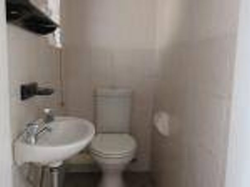 A compact guest bathroom featuring a pedestal washbasin and a standard toilet with neutral wall tiling.