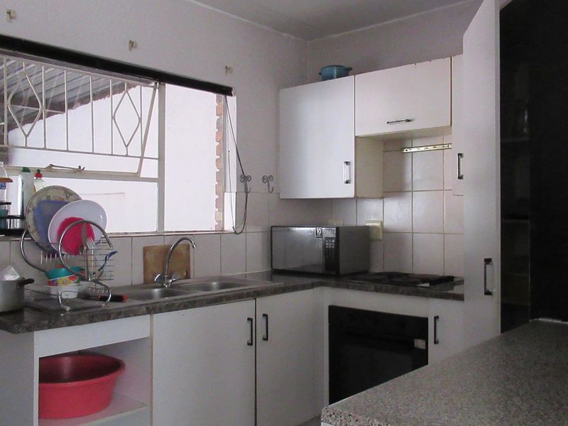 A functional kitchen featuring built-in cabinetry, laminate countertops, a stainless steel double sink, and integrated oven and hob with tiled backsplash.