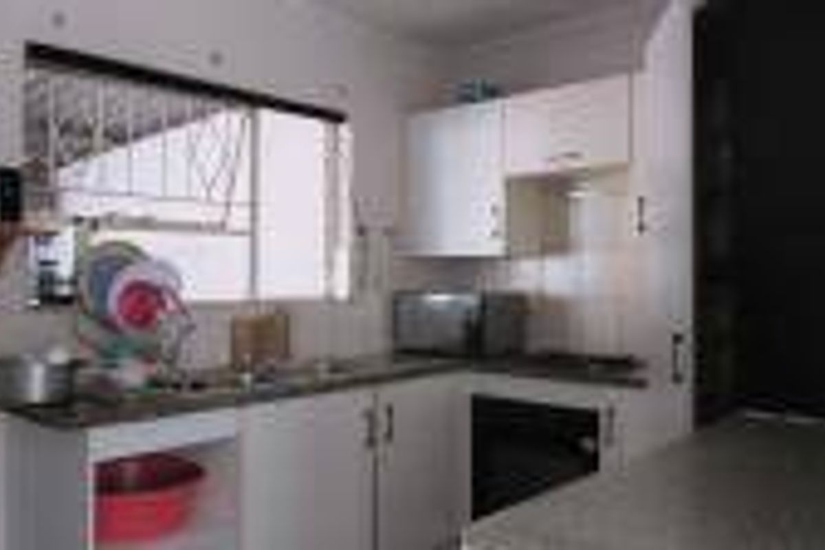 A functional kitchen featuring white cabinetry, laminate countertops, a built-in oven, and a window with security bars.
