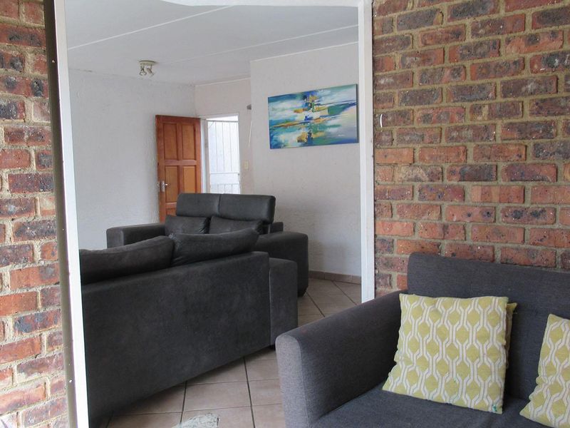A living room area featuring exposed brick walls and tiled flooring, providing a rustic aesthetic with a clear transition between connected living spaces.
