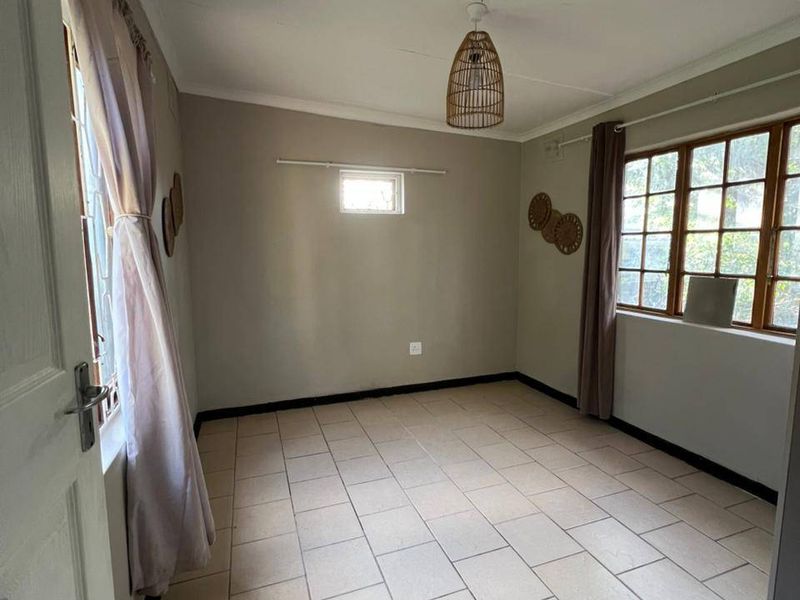 A bright, empty bedroom featuring neutral tiled flooring and timber-framed windows, offering a clean and versatile space ready for personalization.
