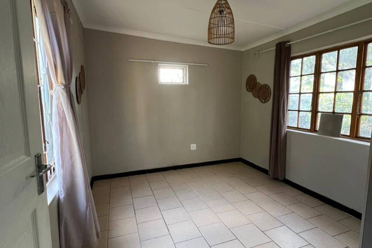 A bright, empty bedroom featuring neutral tiled flooring and timber-framed windows, offering a clean and versatile space ready for personalization.