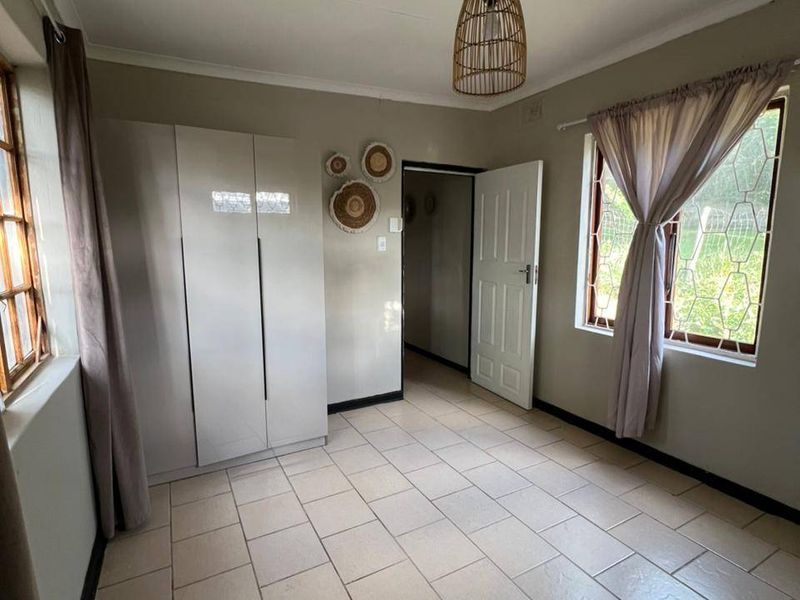 A bright, neutral bedroom featuring tiled flooring, built-in cupboards, and security bars on the windows, offering a clean and functional living space.