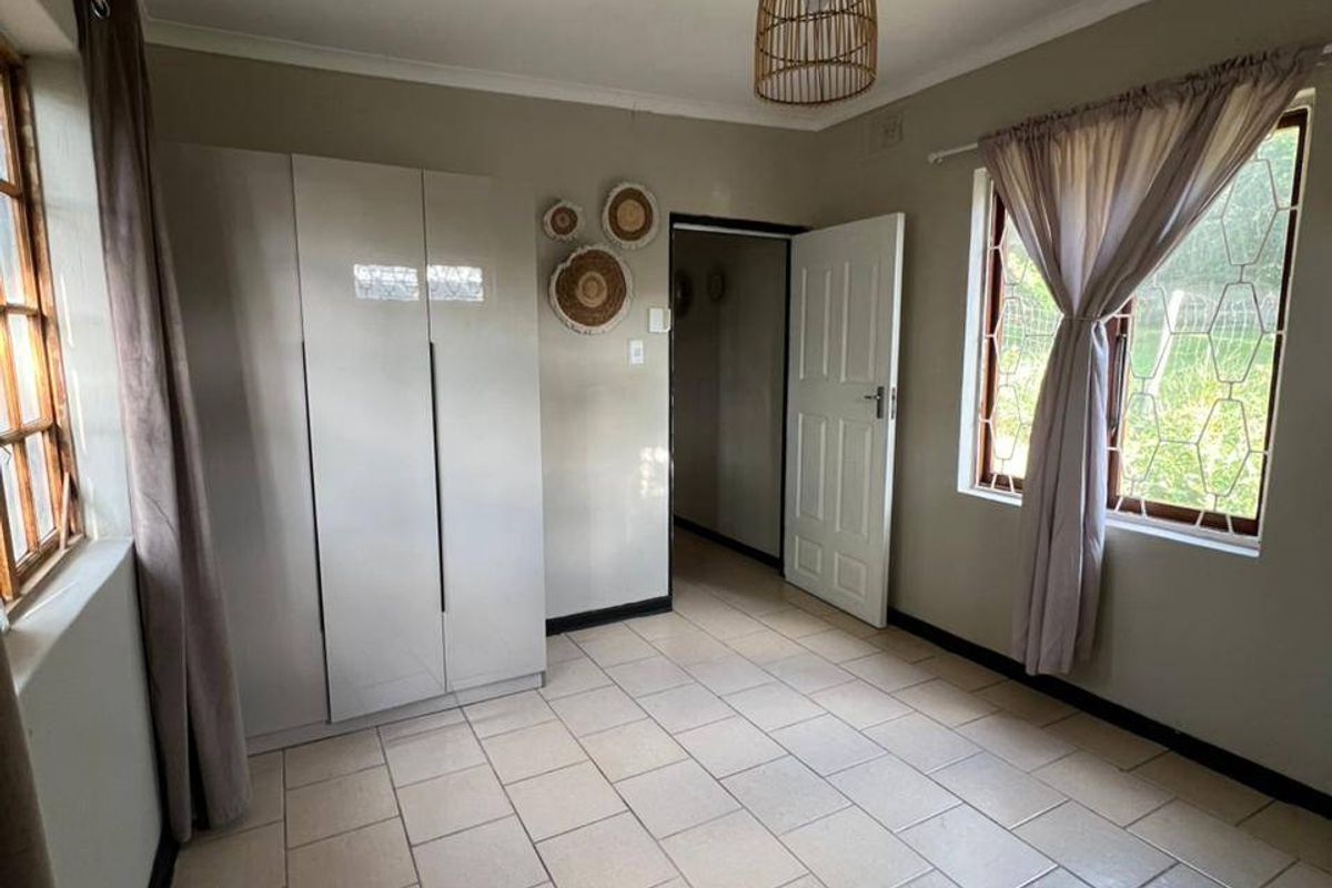 A bright, neutral bedroom featuring tiled flooring, built-in cupboards, and security bars on the windows, offering a clean and functional living space.