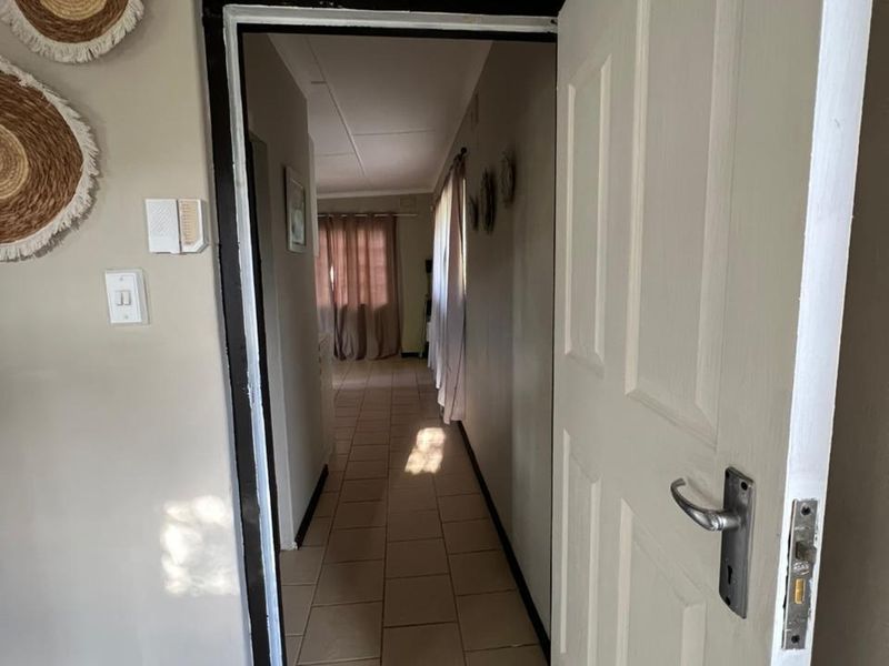 A view through an open doorway into a tiled hallway leading towards a living area with natural light.