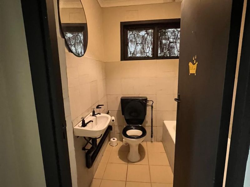 A compact bathroom featuring a wall-mounted basin, toilet, and bathtub with tiled finishes and security bars on the window.