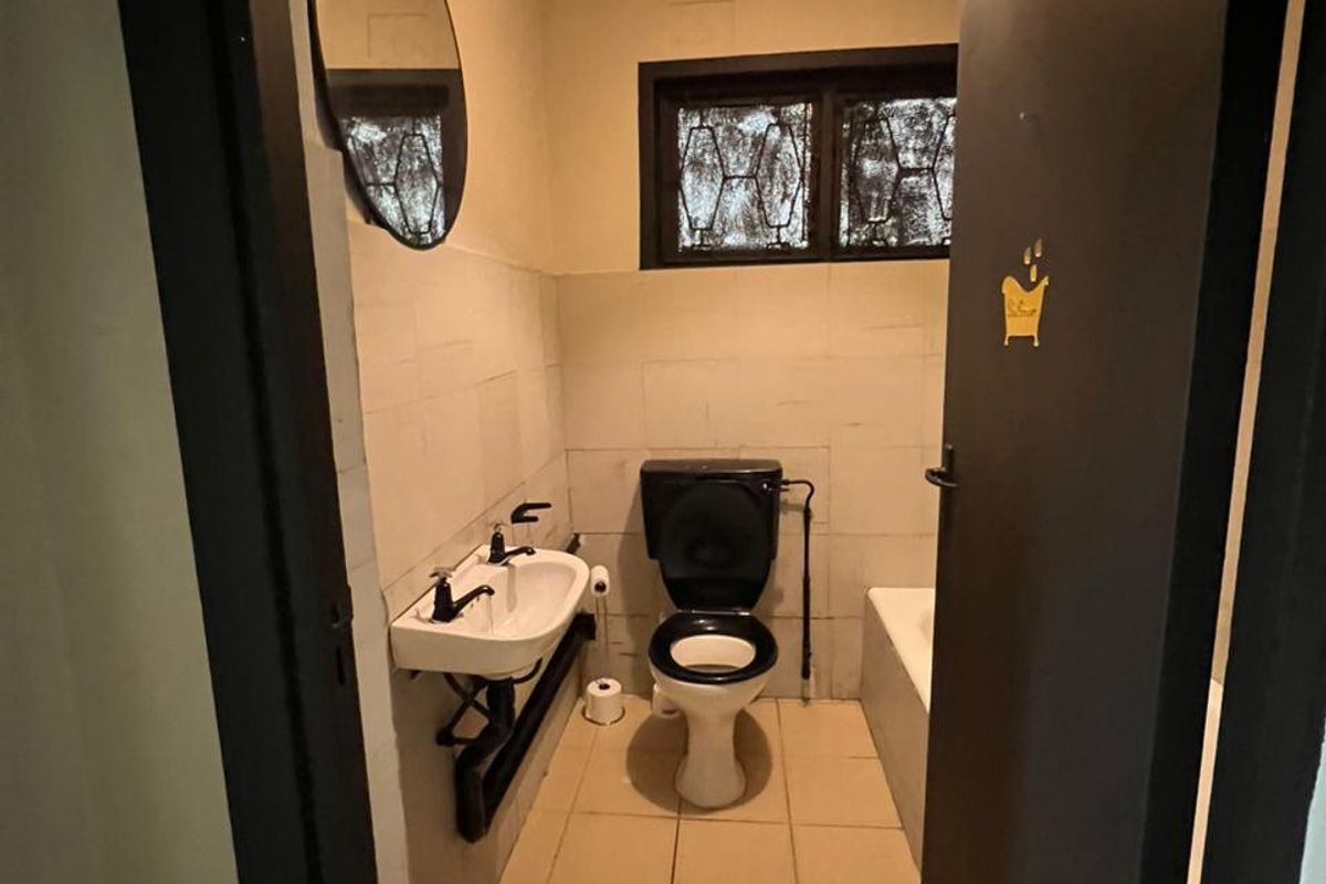 A compact bathroom featuring a wall-mounted basin, toilet, and bathtub with tiled finishes and security bars on the window.