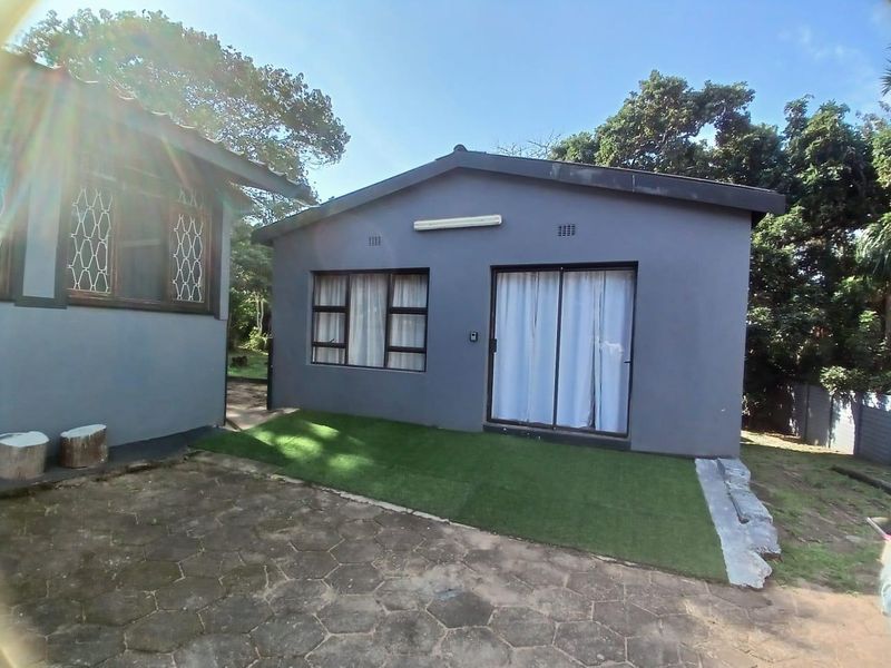 Rear exterior view of the property featuring a paved patio area, artificial lawn, sliding glass doors, and aluminium window frames.