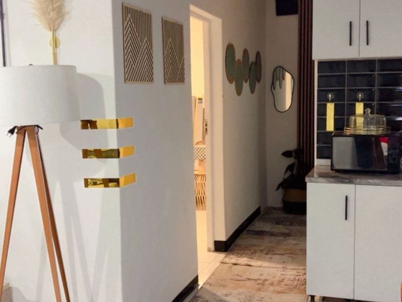 A modern kitchen area featuring white cabinetry, a dark tiled backsplash, and striking exposed timber ceiling beams.