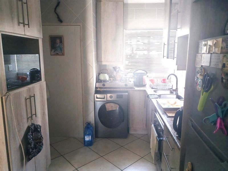Compact kitchen featuring light wood-look cabinetry, tiled flooring, built-in oven, hob, and integrated laundry appliance space with a functional layout.