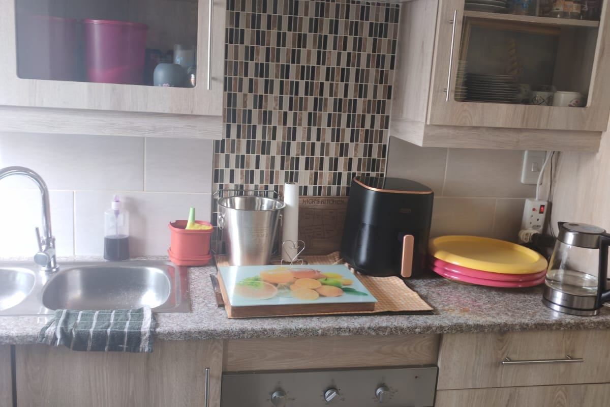 A functional kitchen featuring light wood-grain cabinetry, mosaic tile splashback, stainless steel oven, and ample storage space with integrated sink and countertop area.