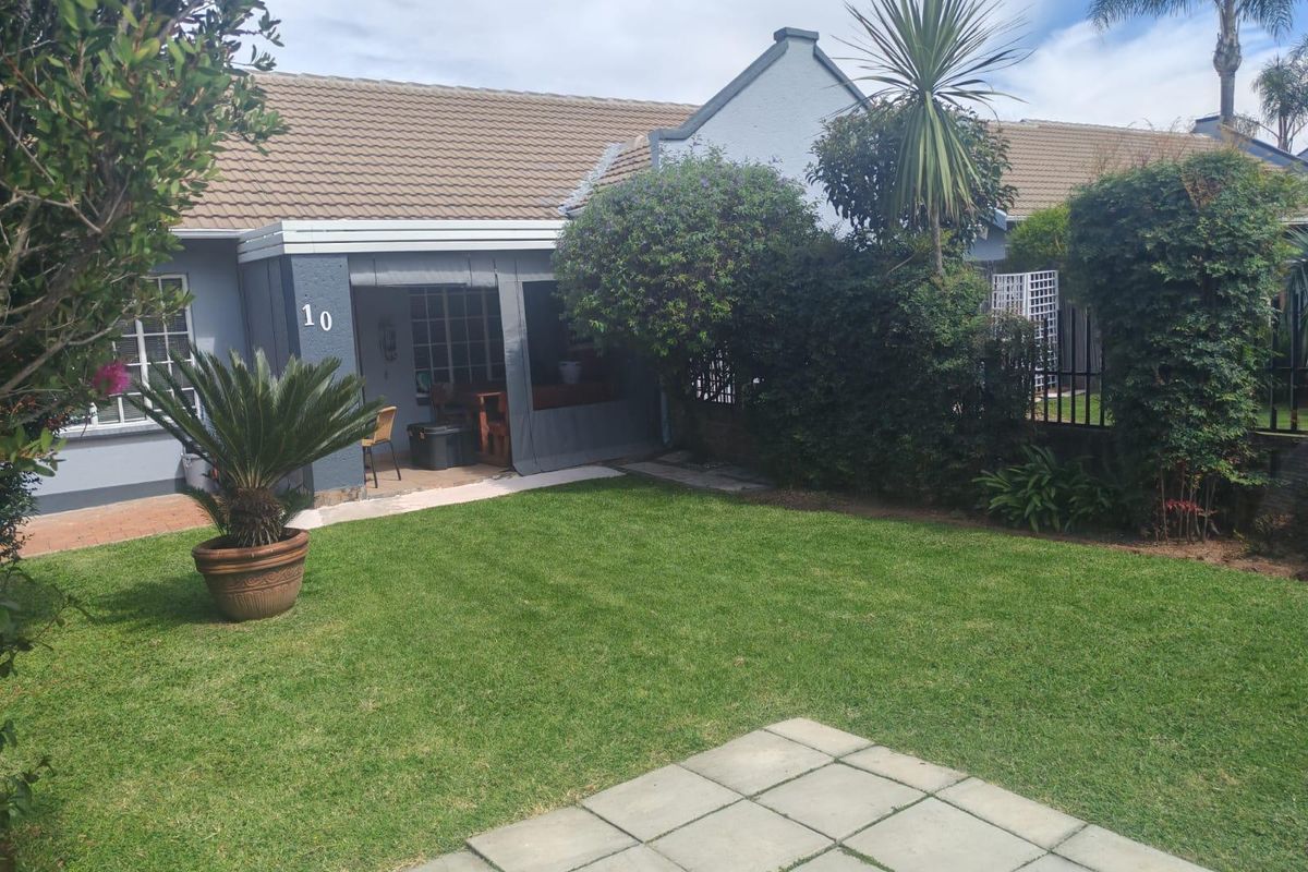 Rear view of the townhouse featuring a well-maintained lawn, paved patio area, and a covered patio space with established garden landscaping.