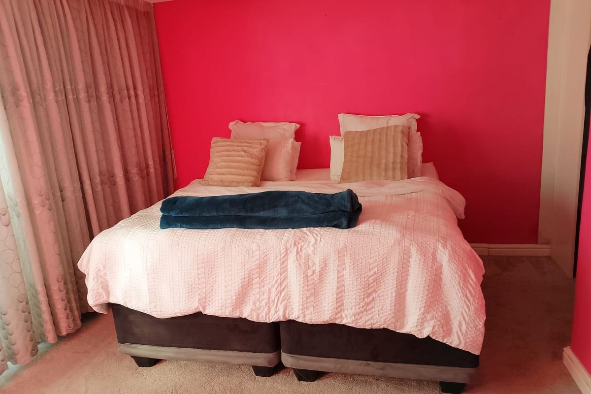 A bedroom featuring carpeted flooring and floor-to-ceiling curtains, currently finished with a bold pink accent wall.
