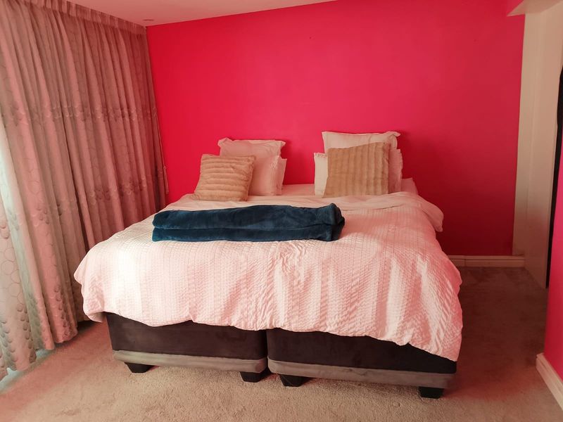 A bedroom featuring carpeted flooring and floor-to-ceiling curtains, currently finished with a bold pink accent wall.