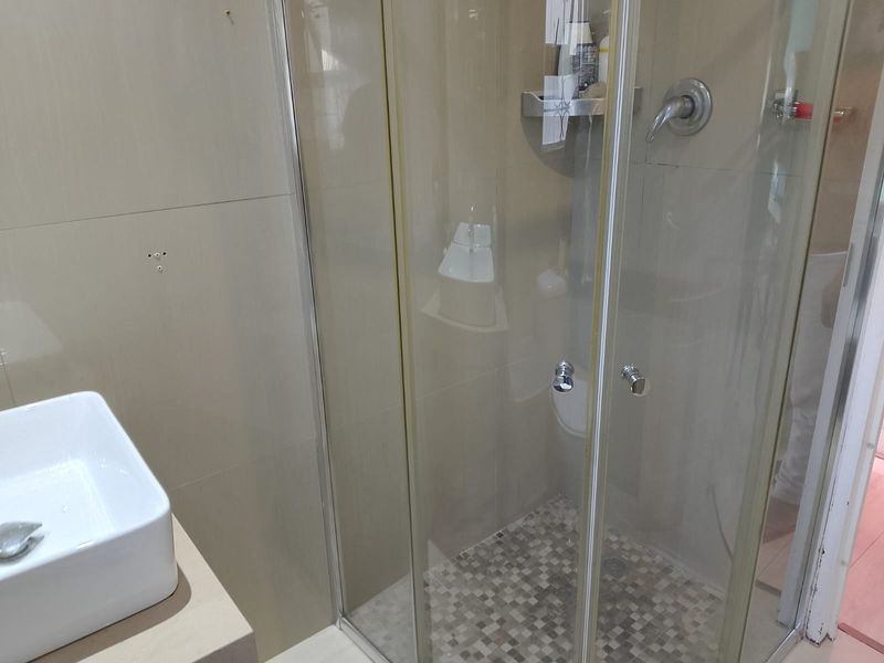 A functional bathroom featuring a glass-enclosed shower with mosaic floor tiling and a modern vessel sink vanity.