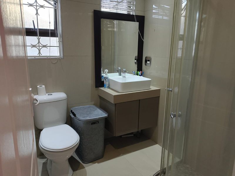 A functional bathroom featuring a modern vessel sink on a vanity cabinet, a toilet, and a glass-enclosed shower with neutral wall and floor tiling.