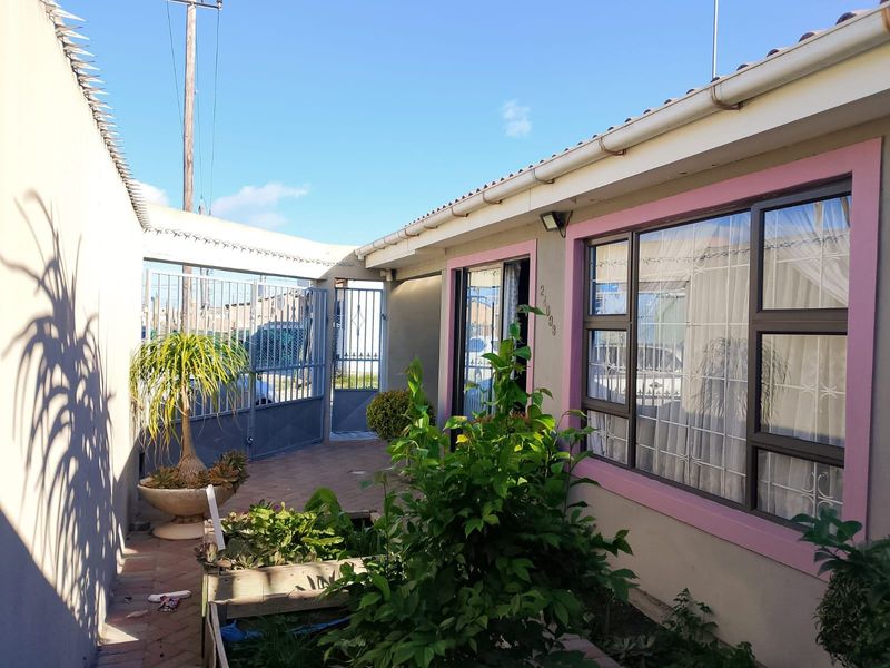 Front entrance area featuring a paved driveway, metal security gate, and aluminium windows with security bars.