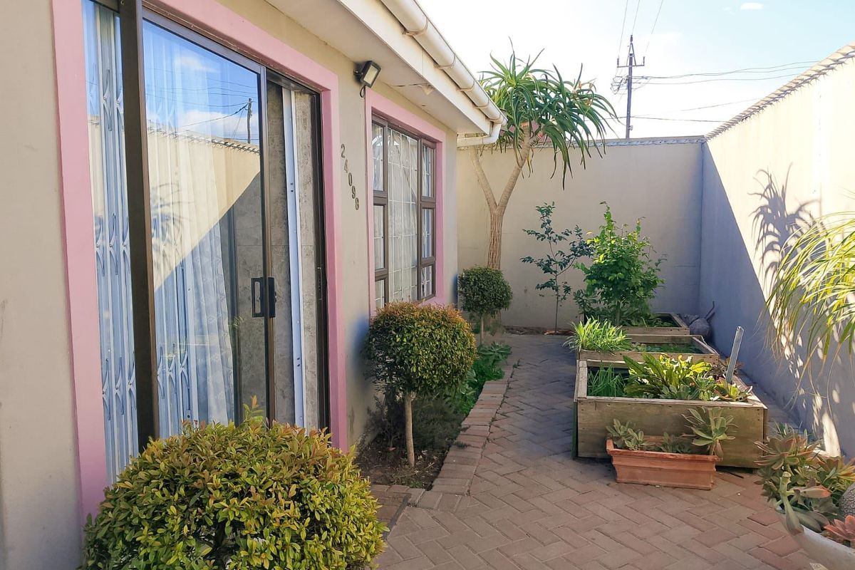 A private rear courtyard featuring brick paving, raised garden beds, and direct access to the home via a sliding glass door.